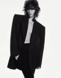 Model with dark shaggy hair wearing an oversized black blazer against a white seamless background