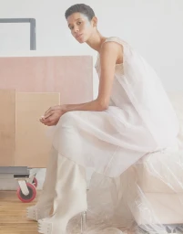 Model with short dark hair seated in a white sheer dress and tall boots styled by Joanne Blades