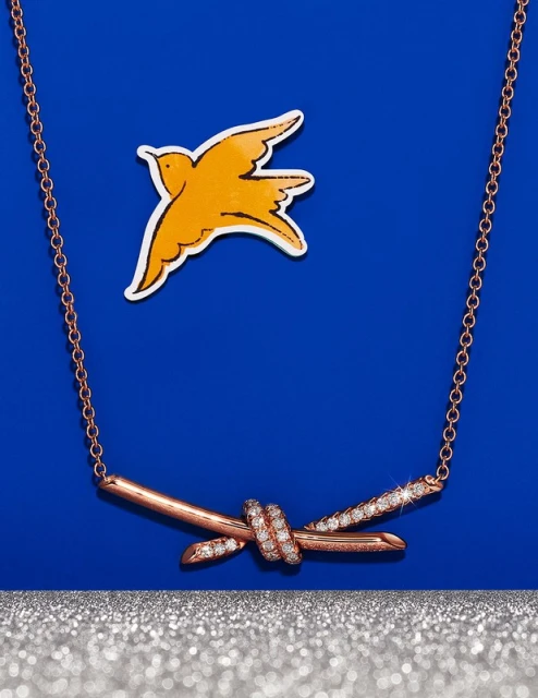 Close-up studio shot of a rose gold necklace featuring a 'barbed wire' design with diamond accents, set against a blue backdrop.