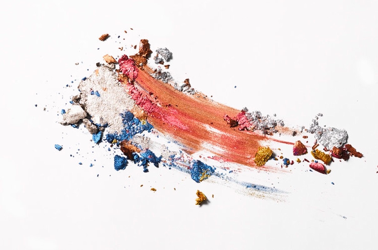 Close-up of vibrant makeup swatches including shades of bronze, pink, silver, gold, and blue on a white background, cosmetics concept.
