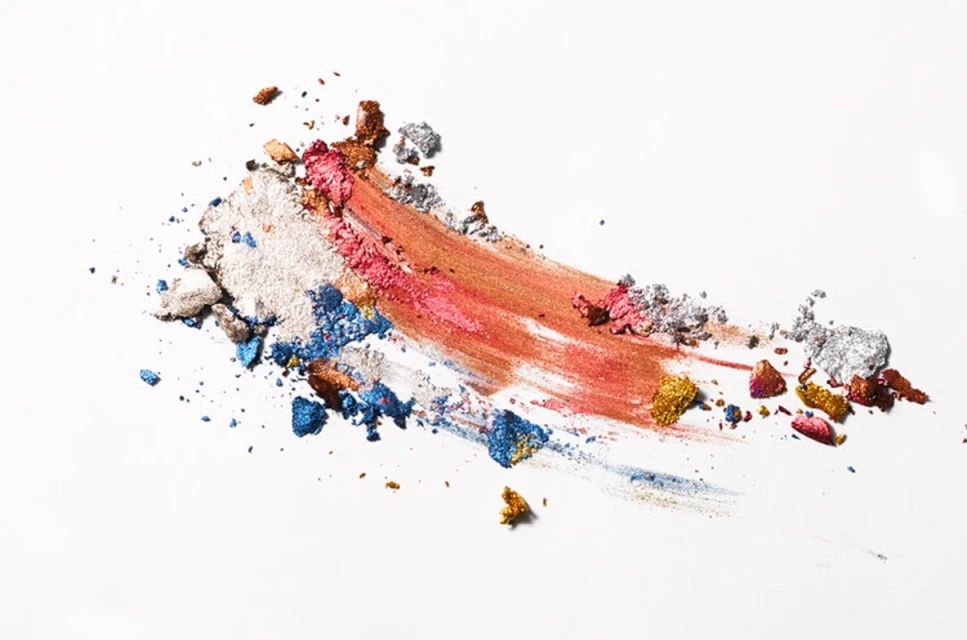 Close-up of vibrant makeup swatches including shades of bronze, pink, silver, gold, and blue on a white background, cosmetics concept.