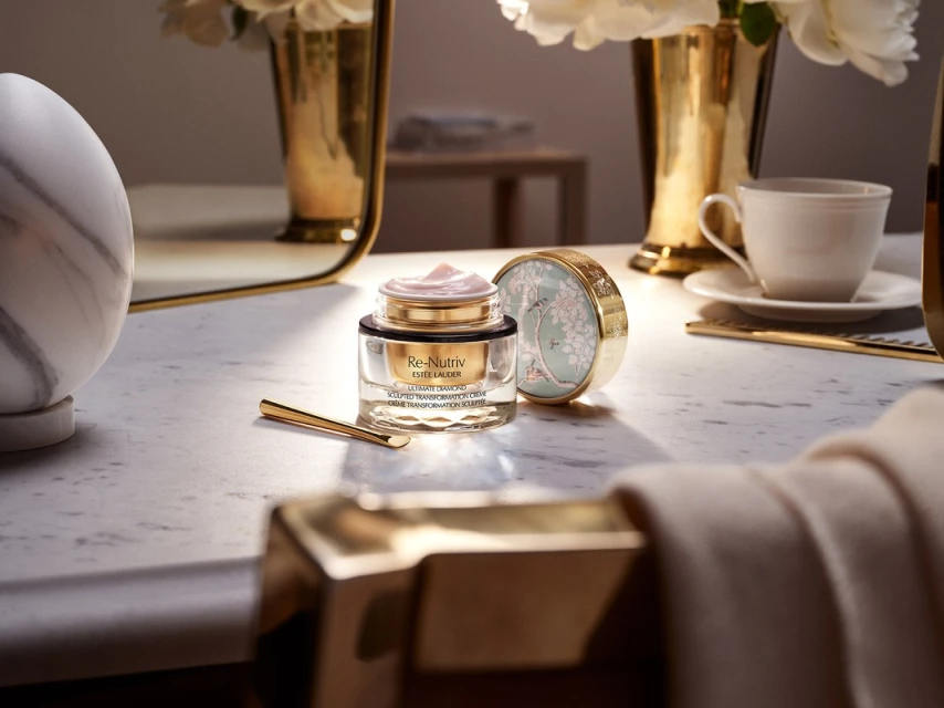 Elegant beauty product still life: Re-Nutriv cream with gold accents, flowers, marble, and tea cup create a luxurious beauty scene.
