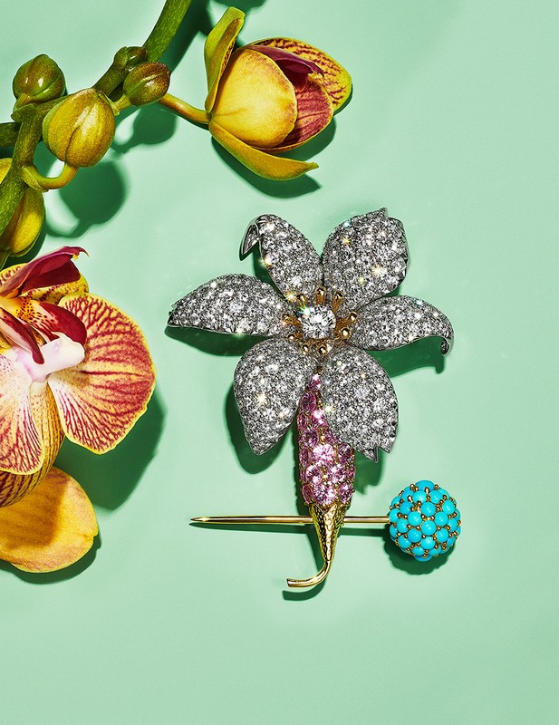 Close-up of a flower-shaped diamond brooch with a turquoise sphere and orchid blossoms on a light green background, jewelry product shot.