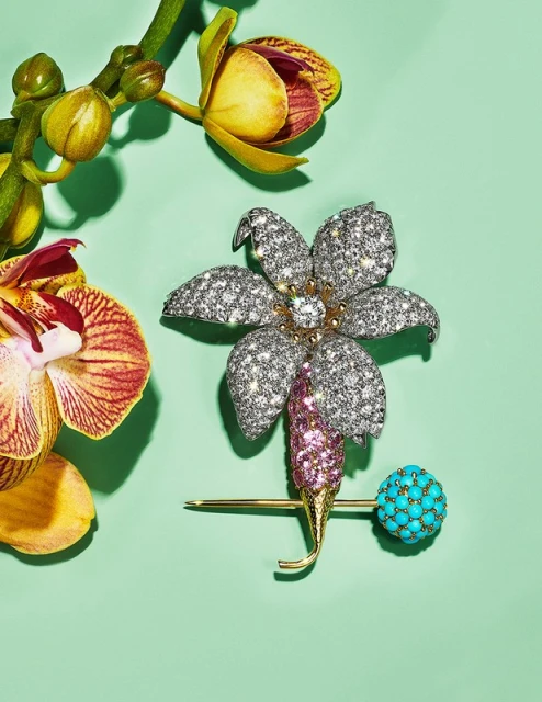Close-up of a flower-shaped diamond brooch with a turquoise sphere and orchid blossoms on a light green background, jewelry product shot.