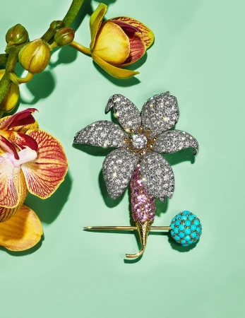 Close-up of a flower-shaped diamond brooch with a turquoise sphere and orchid blossoms on a light green background, jewelry product shot.