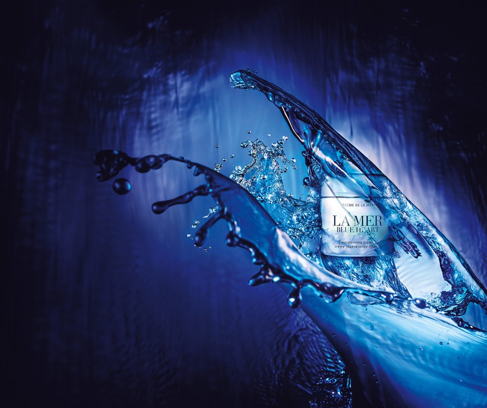 La Mer cream jar surrounded by a blue water splash against a dark blue background in a beauty and skincare product shot.