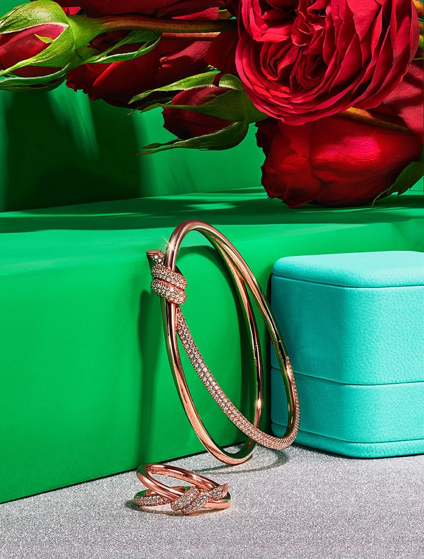 Rose gold bracelet and ring jewelry set with diamonds on a silver surface, set against a green and turquoise background with roses.