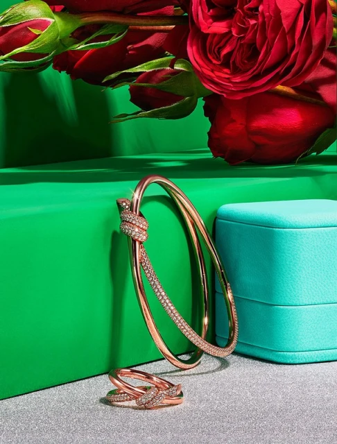 Rose gold bracelet and ring jewelry set with diamonds on a silver surface, set against a green and turquoise background with roses.