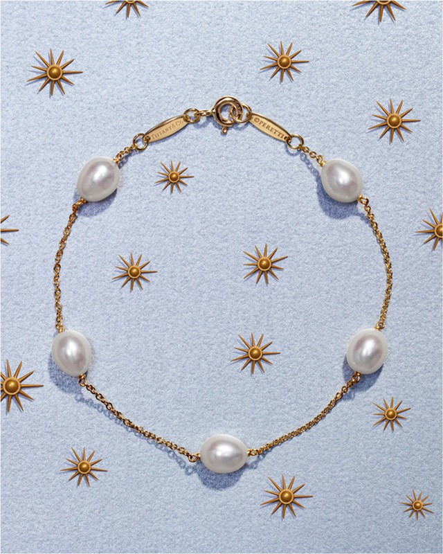 Overhead shot of a gold chain bracelet featuring freshwater pearls on a light blue surface with gold sunburst decorations.