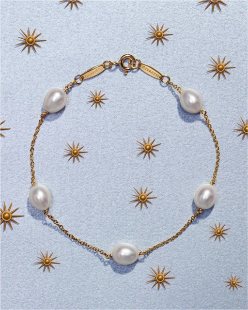 Overhead shot of a gold chain bracelet featuring freshwater pearls on a light blue surface with gold sunburst decorations.