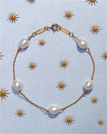 Overhead shot of a gold chain bracelet featuring freshwater pearls on a light blue surface with gold sunburst decorations.