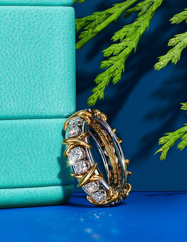Close-up of a diamond eternity band in silver and gold, styled with a turquoise jewelry box and cedar sprigs against a blue backdrop.