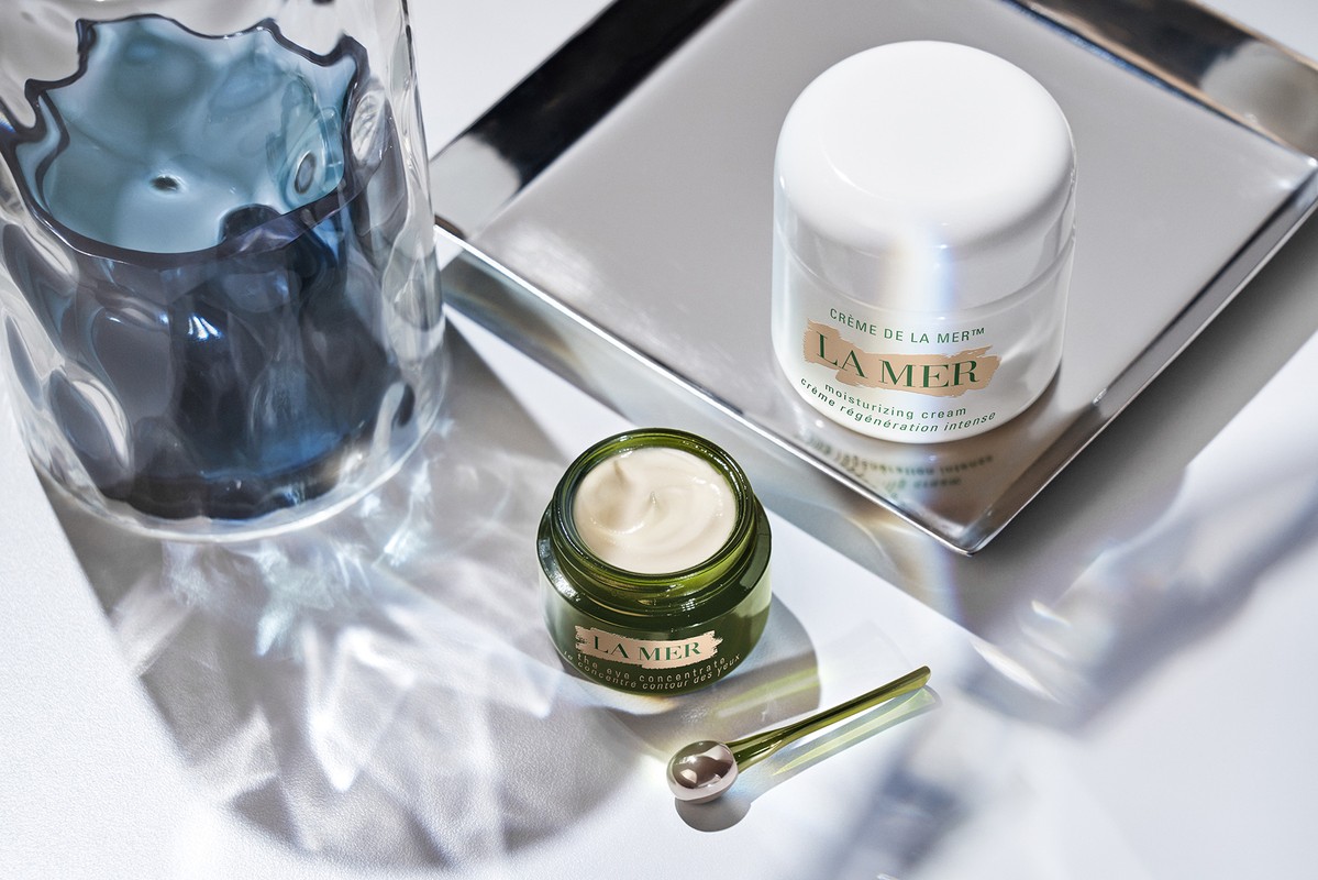 La Mer skincare product set on a silver tray, featuring a jar of cream, open container, and applicator, against a white background.