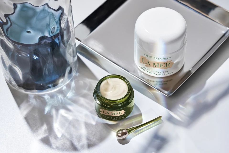 La Mer skincare product set on a silver tray, featuring a jar of cream, open container, and applicator, against a white background.