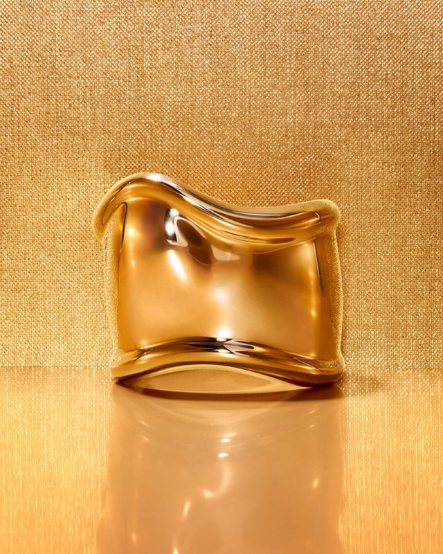 Gold-colored metal bracelet on a reflective gold surface against a textured gold backdrop creating a luxurious and elegant visual.