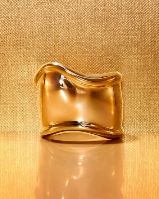 Gold-colored metal bracelet on a reflective gold surface against a textured gold backdrop creating a luxurious and elegant visual.