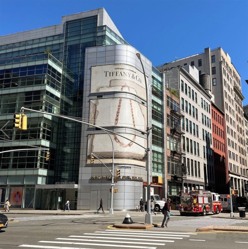 Cityscape featuring a Tiffany & Co. advertisement on a modern building, traffic lights, pedestrian crosswalks, and an emergency vehicle.