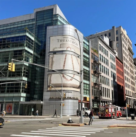 Cityscape featuring a Tiffany & Co. advertisement on a modern building, traffic lights, pedestrian crosswalks, and an emergency vehicle.
