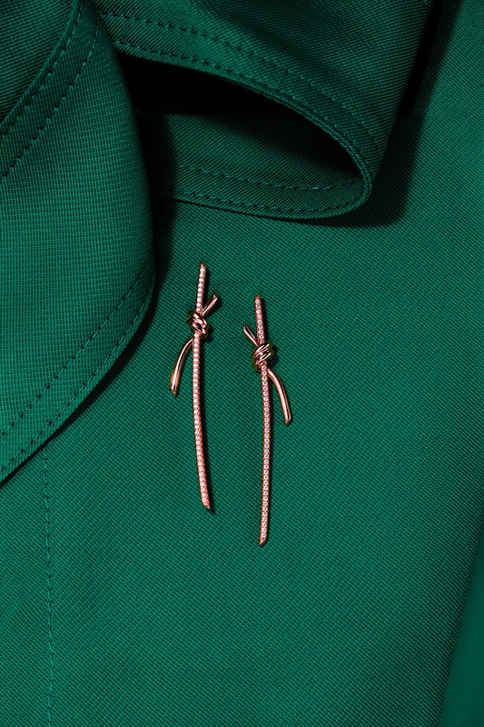 Elegant knot-shaped dangle earrings with gemstone details displayed on a deep green fabric background, showcasing a high-fashion jewelry design.