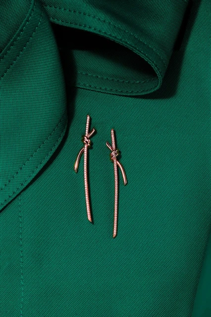 Elegant knot-shaped dangle earrings with gemstone details displayed on a deep green fabric background, showcasing a high-fashion jewelry design.