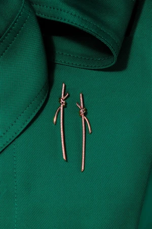 Elegant knot-shaped dangle earrings with gemstone details displayed on a deep green fabric background, showcasing a high-fashion jewelry design.
