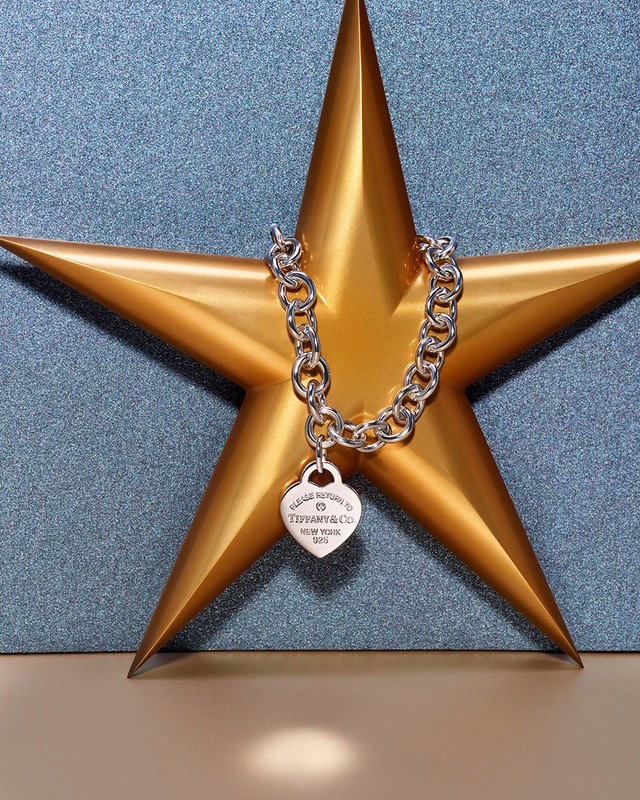 Silver Tiffany & Co heart pendant necklace on a gold star against a textured blue background in a close-up studio shot.