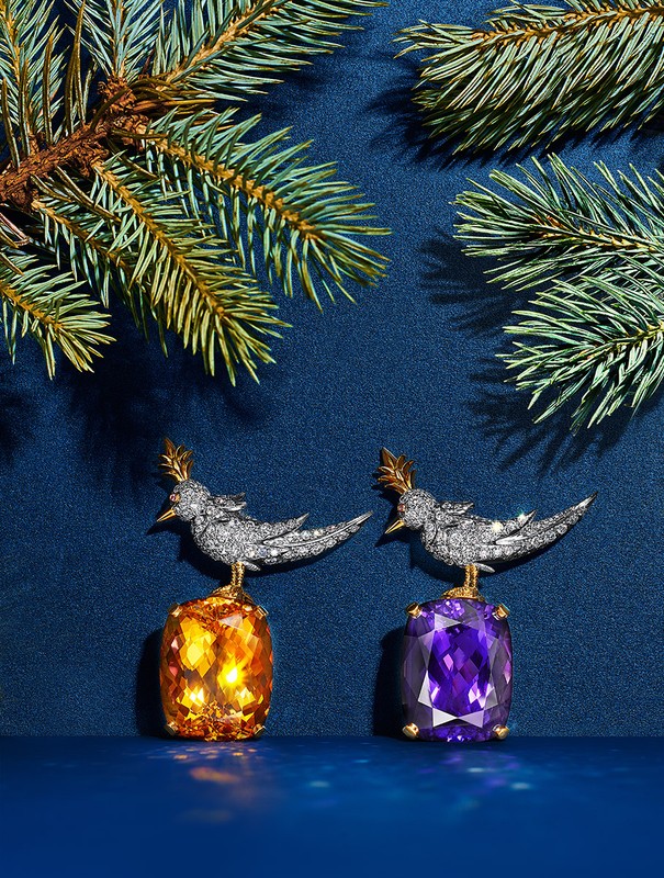 Two bird figurines, crafted with gemstones and diamonds, perch on faceted amethyst and citrine stones against a deep blue background.