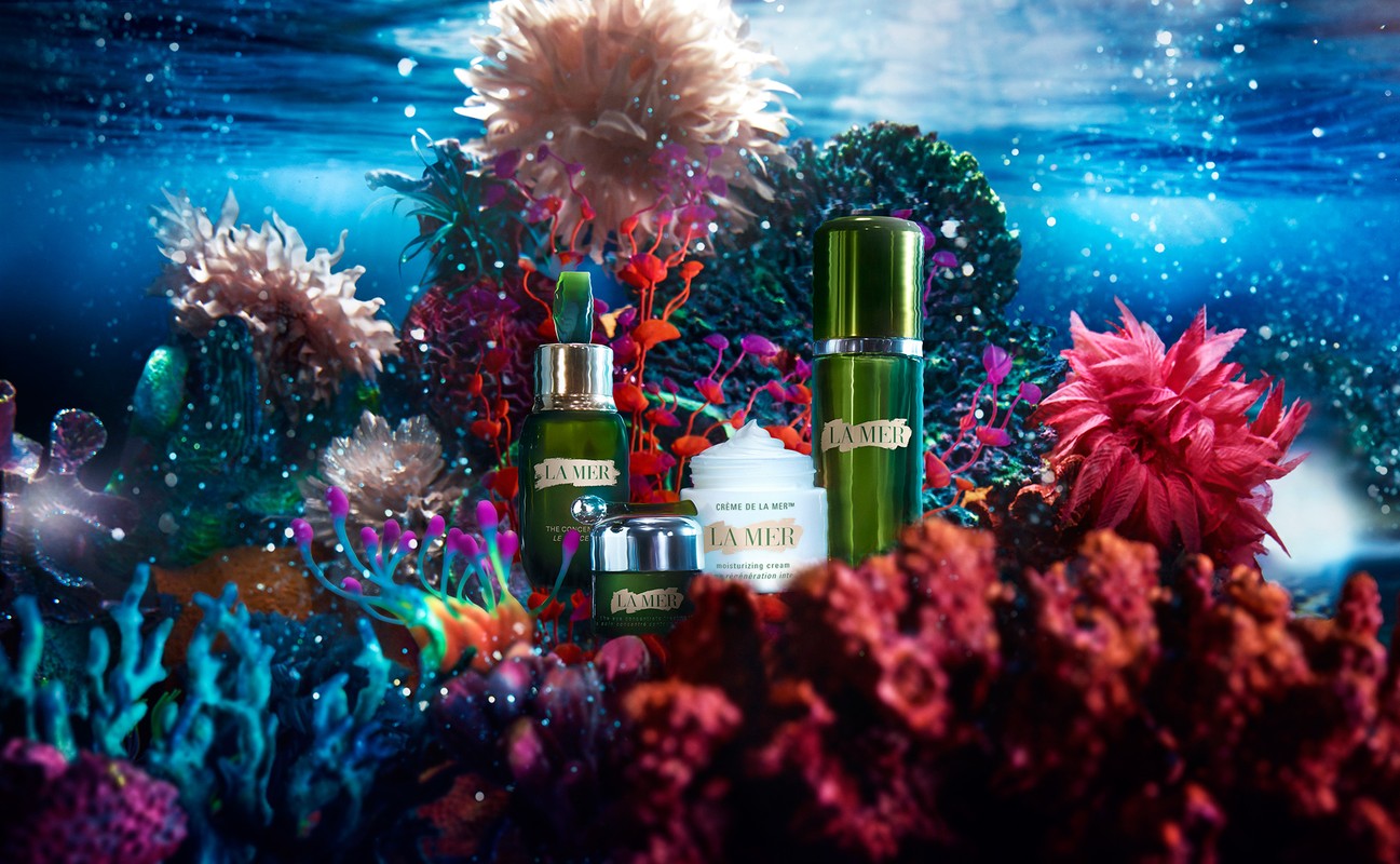 La Mer skincare products are displayed against a backdrop of vibrant coral and blue underwater lighting, creating a luxurious, ocean-themed aesthetic.