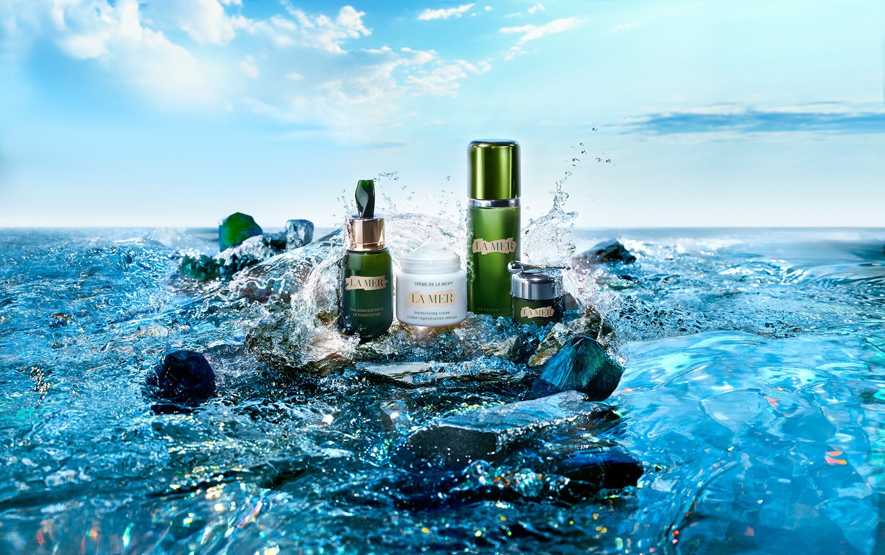 La Mer skincare product line is displayed amidst splashing water and rocks, set against a backdrop of the sky and ocean.