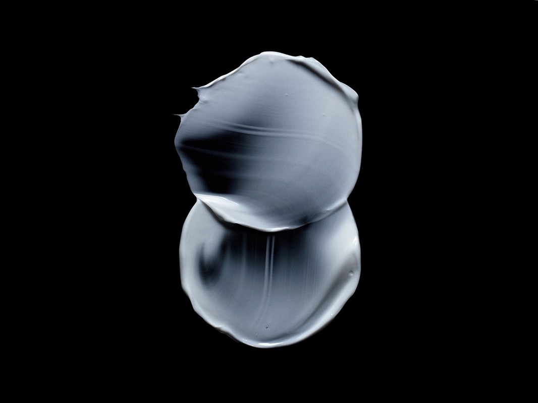 Close-up of a smear of gray cream with a shiny finish against a black background, creating a minimalist and graphic composition.
