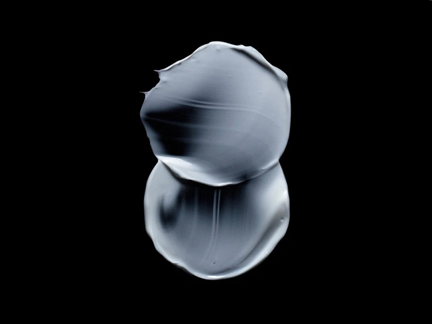 Close-up of a smear of gray cream with a shiny finish against a black background, creating a minimalist and graphic composition.