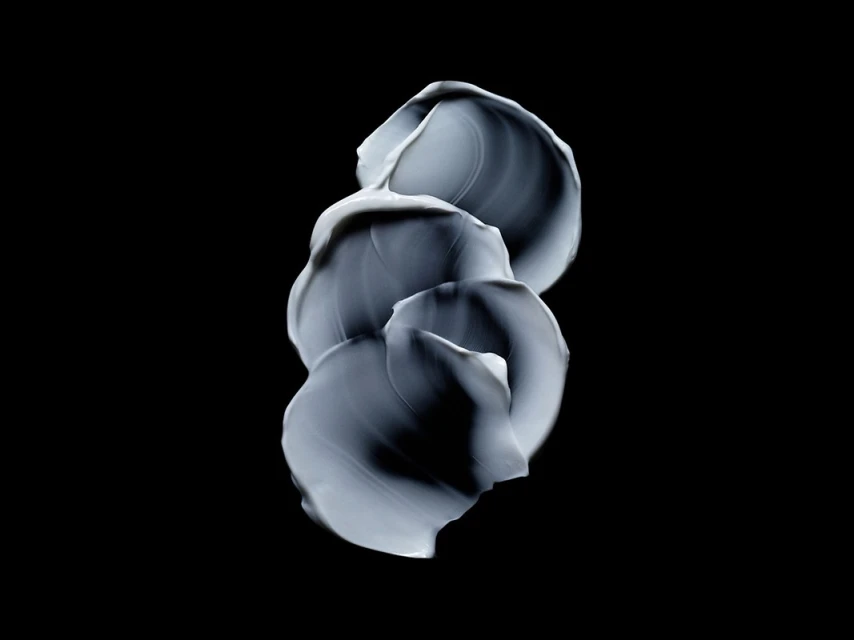 Close-up studio shot of layered swirls of light grey cream against a stark black background, highlighting textures and minimalist design.
