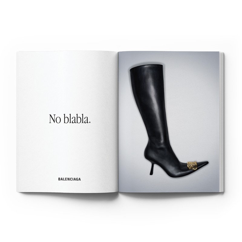Fashion editorial shot of black Balenciaga stiletto boot on white studio background with a spread from a luxury fashion magazine.