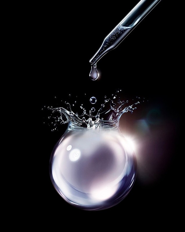 Dropper dispensing liquid into orb causing a splash against black background. Liquid textures create a clean, bright, and modern aesthetic.