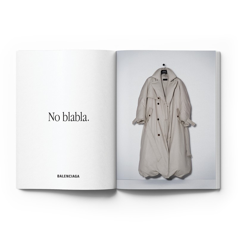 Fashion editorial featuring a Balenciaga trench coat hanging on a white wall, photographed in an open book with accompanying text.