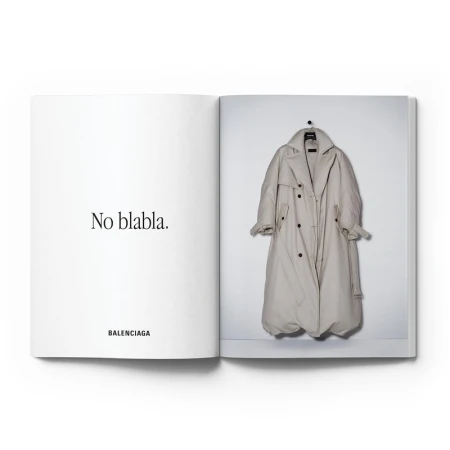 Fashion editorial featuring a Balenciaga trench coat hanging on a white wall, photographed in an open book with accompanying text.