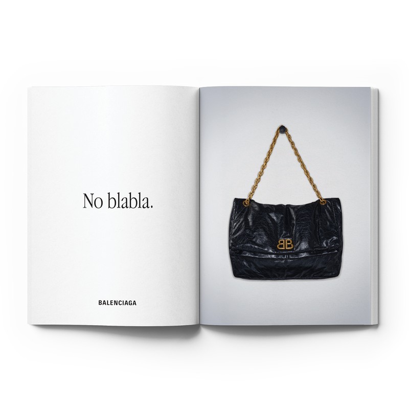 Open magazine displaying a black Balenciaga shoulder bag with a gold chain strap and Balenciaga logo on a white background.
