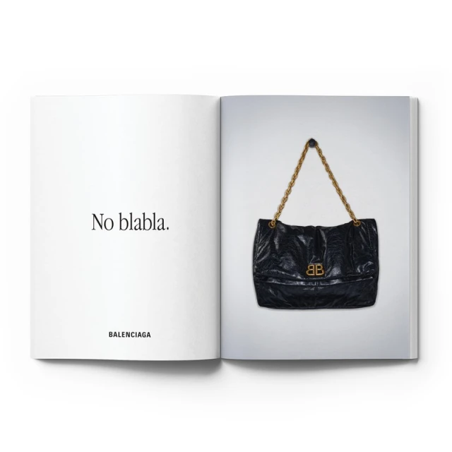 Open magazine displaying a black Balenciaga shoulder bag with a gold chain strap and Balenciaga logo on a white background.