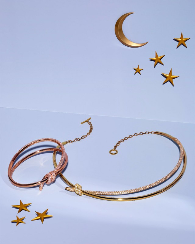 Close-up of gold jewelry including a choker and bracelet on a light blue surface with paper crescent moon and star shapes in the background.