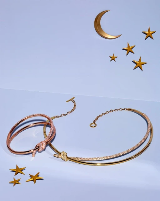 Close-up of gold jewelry including a choker and bracelet on a light blue surface with paper crescent moon and star shapes in the background.