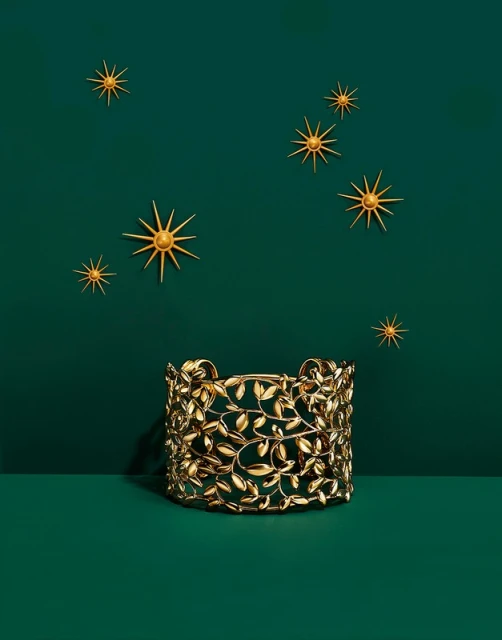 Elegant gold cuff bracelet with leaf details showcased against a dark green backdrop with star-shaped decorations.