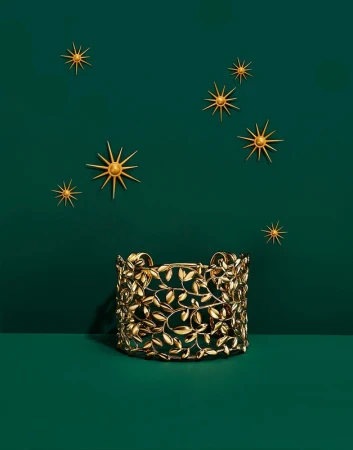 Elegant gold cuff bracelet with leaf details showcased against a dark green backdrop with star-shaped decorations.