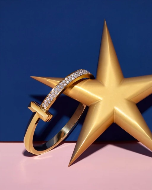 A gold bracelet with diamonds draped over a gold star on a color-blocked pink and blue background, highlighting the jewelry.