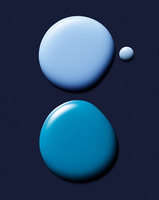 Abstract still life of three drops of different shades of light blue liquid against a dark blue background, close-up studio shot.