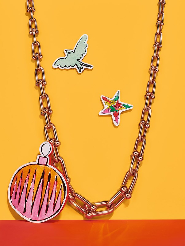 Chain necklace with paper ornaments against a yellow and red background. Statement jewelry with playful, colorful decorations.