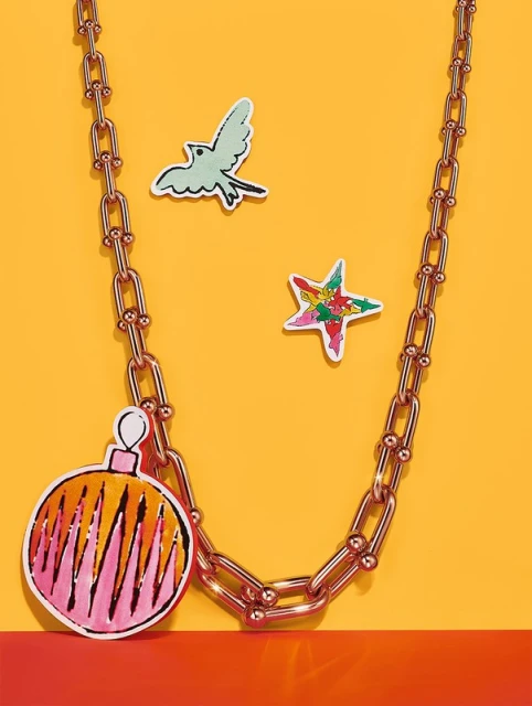 Chain necklace with paper ornaments against a yellow and red background. Statement jewelry with playful, colorful decorations.