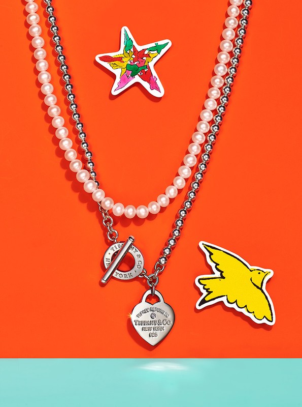 Close-up of a Tiffany & Co. heart pendant necklace with pearl and beaded chains, along with colorful star and bird stickers.