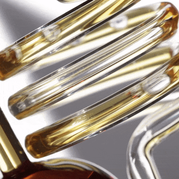 Close-up of clear and gold-tinted glass tubes arranged in a spiral pattern against a white background, casting soft shadows.