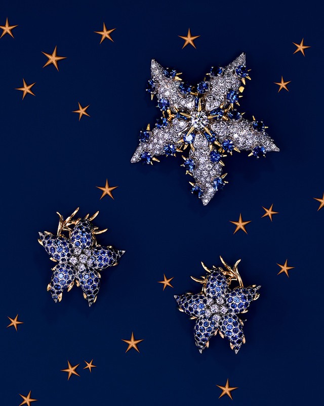 Three star-shaped brooches with white and blue gemstone embellishments on a blue background with small star graphics scattered.