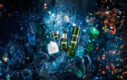 La Mer skincare bottles and jars resting amongst glittering blue and green crystalline water and floating confetti.